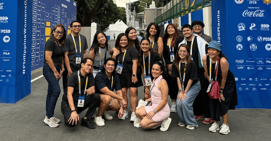A group of about fifteen people posing for a photo outdoors in front of a blue Philippine Women's Open event backdrop.
